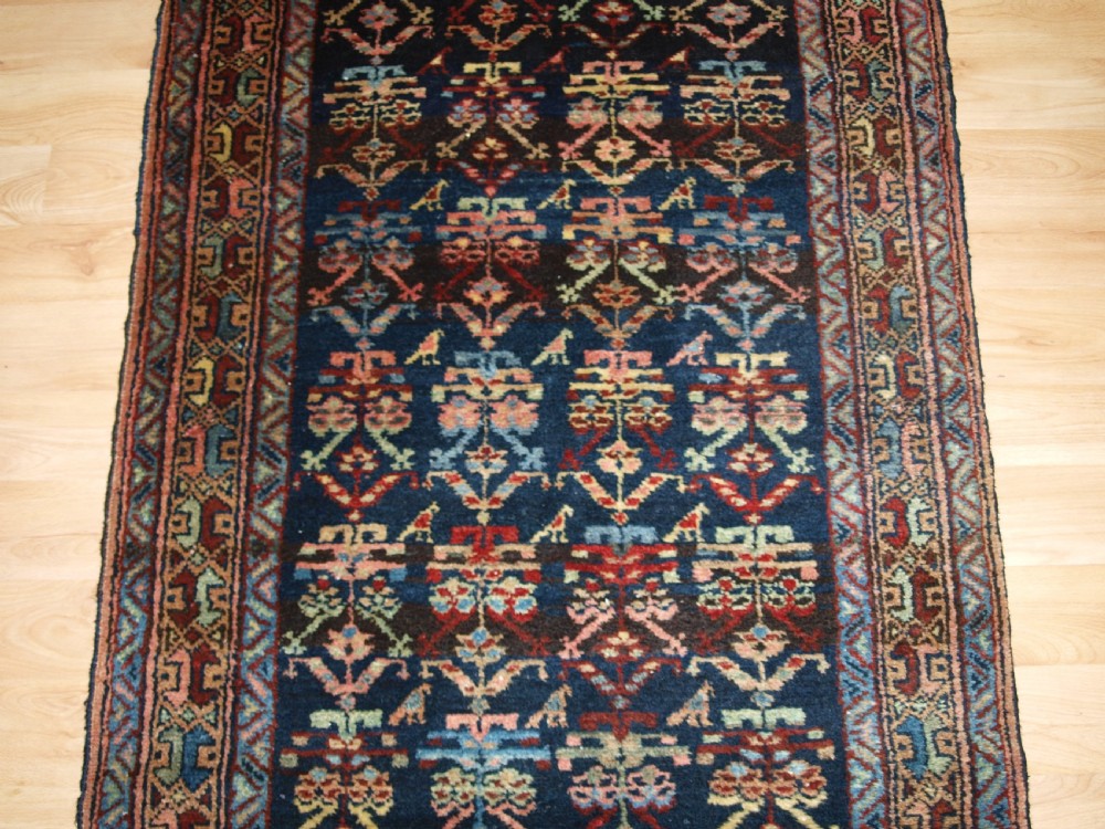 A long narrow antique Luri wool runner carpet with repeating colourful geometric tribal motifs on a dark indigo background framed by decorative multi-band borders. View V