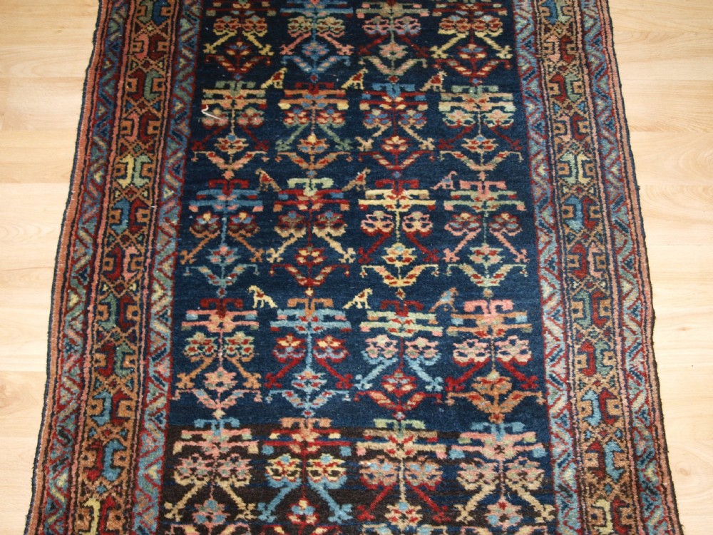 A long narrow antique Luri wool runner carpet with repeating colourful geometric tribal motifs on a dark indigo background framed by decorative multi-band borders. View VI