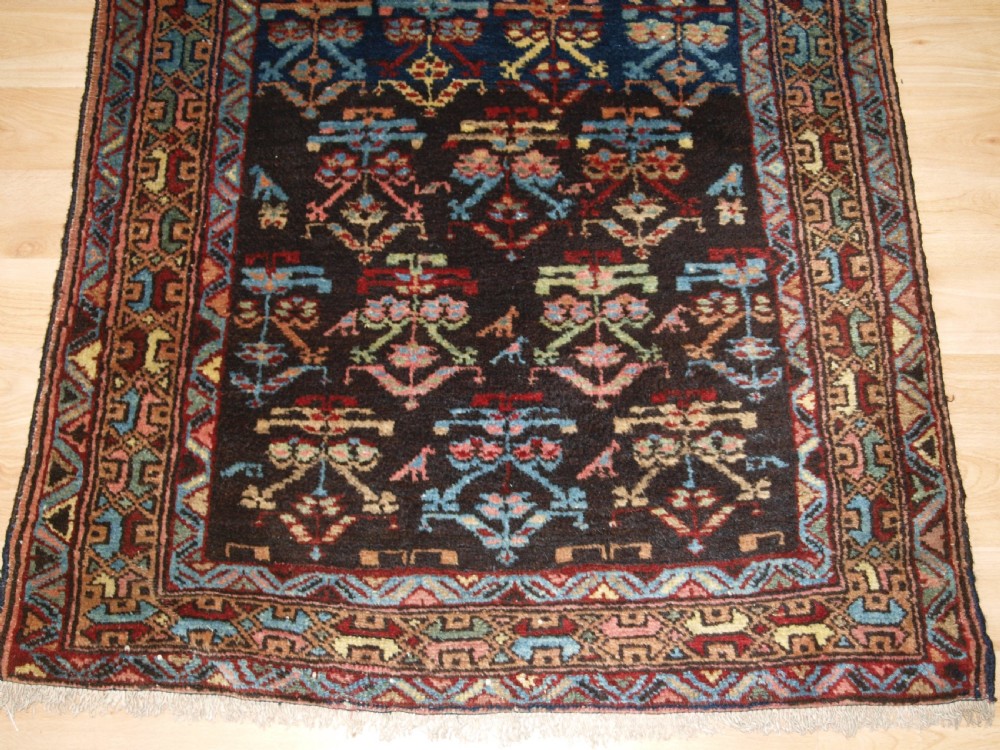 A long narrow antique Luri wool runner carpet with repeating colourful geometric tribal motifs on a dark indigo background framed by decorative multi-band borders. View VIII