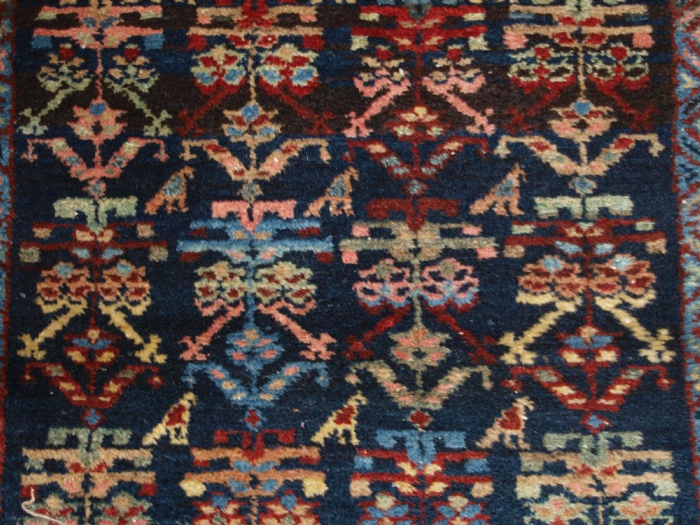 A long narrow antique Luri wool runner carpet with repeating colourful geometric tribal motifs on a dark indigo background framed by decorative multi-band borders. View X