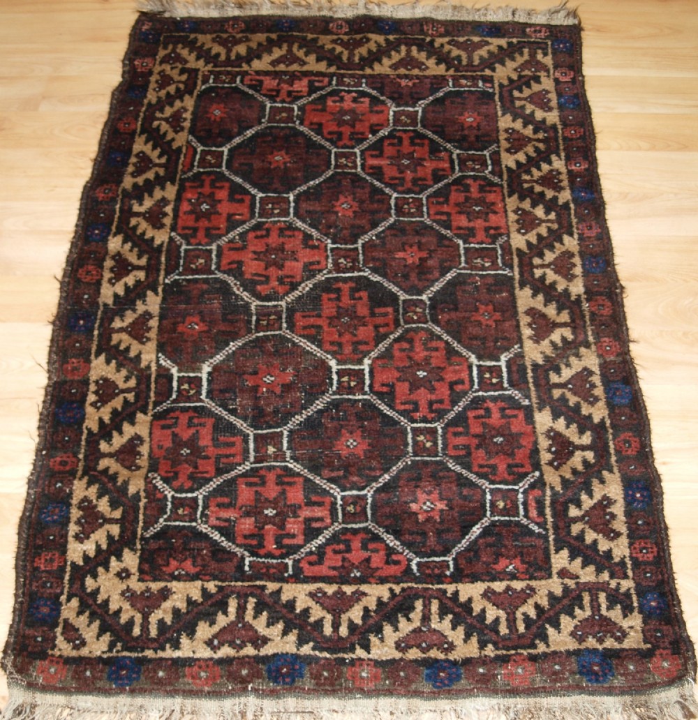 An antique Afghan Baluch wool rug featuring a dark red and brown diamond lattice design framed by geometric serrated borders.