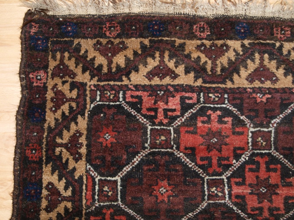 An antique Afghan Baluch wool rug featuring a dark red and brown diamond lattice design framed by geometric serrated borders. View III