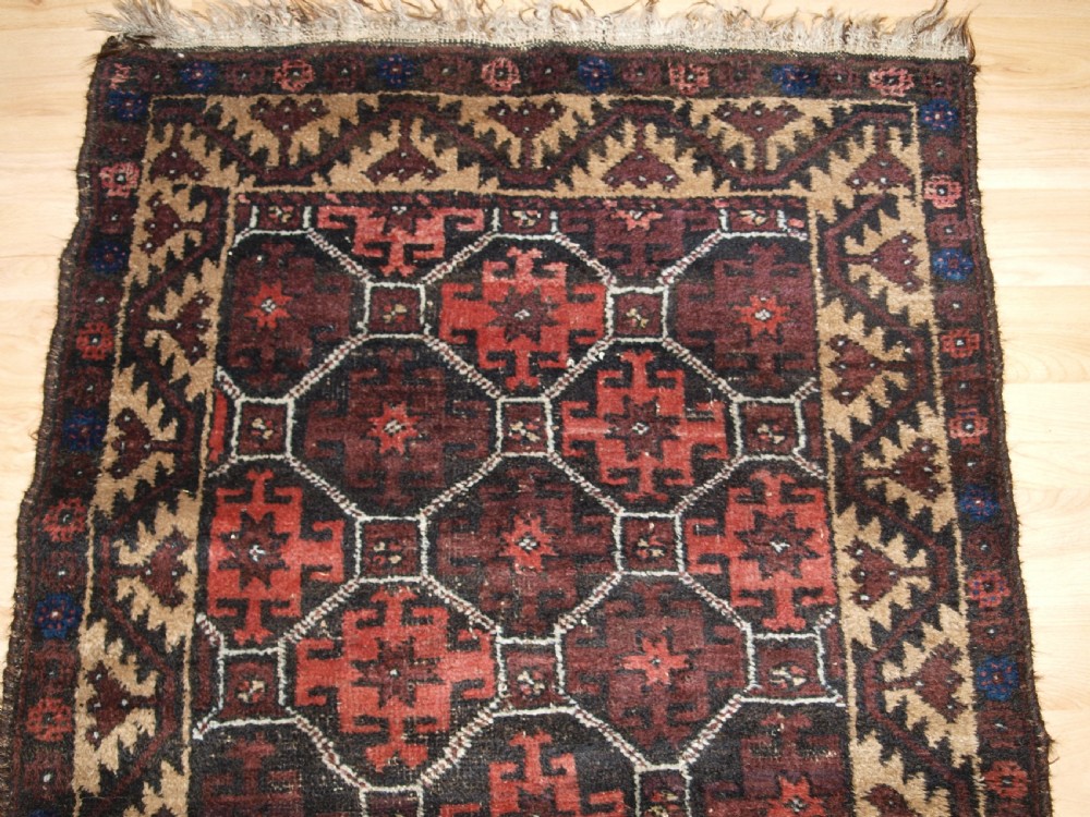An antique Afghan Baluch wool rug featuring a dark red and brown diamond lattice design framed by geometric serrated borders. View IV