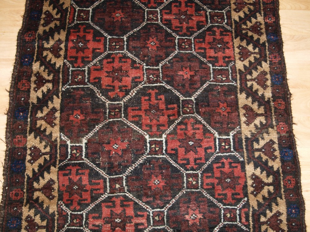 An antique Afghan Baluch wool rug featuring a dark red and brown diamond lattice design framed by geometric serrated borders. View V