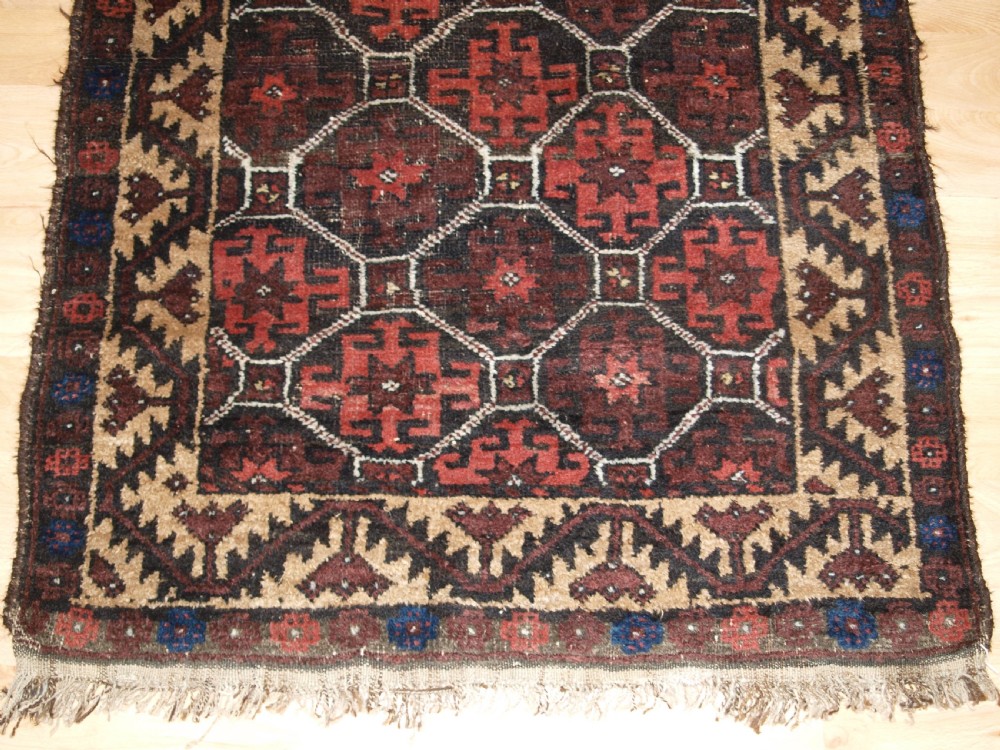 An antique Afghan Baluch wool rug featuring a dark red and brown diamond lattice design framed by geometric serrated borders. View VI