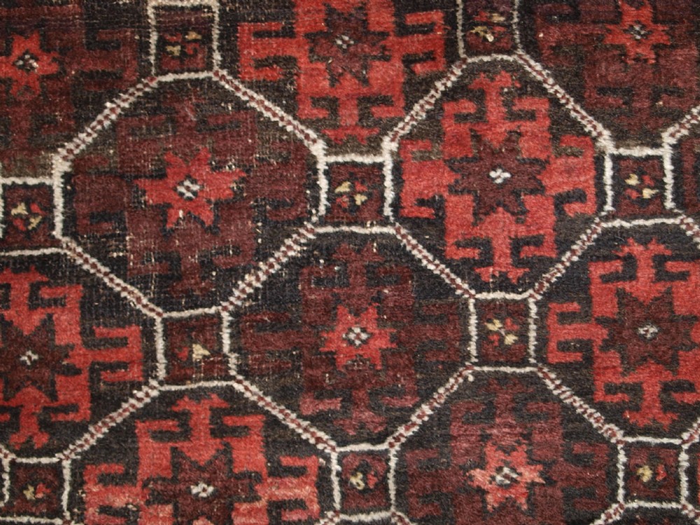 An antique Afghan Baluch wool rug featuring a dark red and brown diamond lattice design framed by geometric serrated borders. View VII