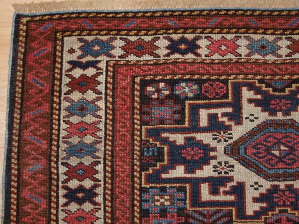 An antique Caucasian hand-knotted wool rug with geometric Lesghi star medallions on a cream field surrounded by patterned borders in red, navy, and ivory. View II