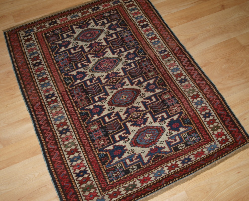 An antique Caucasian hand-knotted wool rug with geometric Lesghi star medallions on a cream field surrounded by patterned borders in red, navy, and ivory. View III