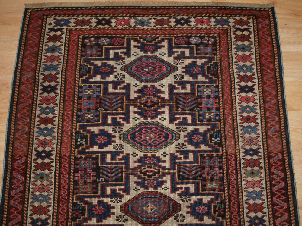 An antique Caucasian hand-knotted wool rug with geometric Lesghi star medallions on a cream field surrounded by patterned borders in red, navy, and ivory. View IV
