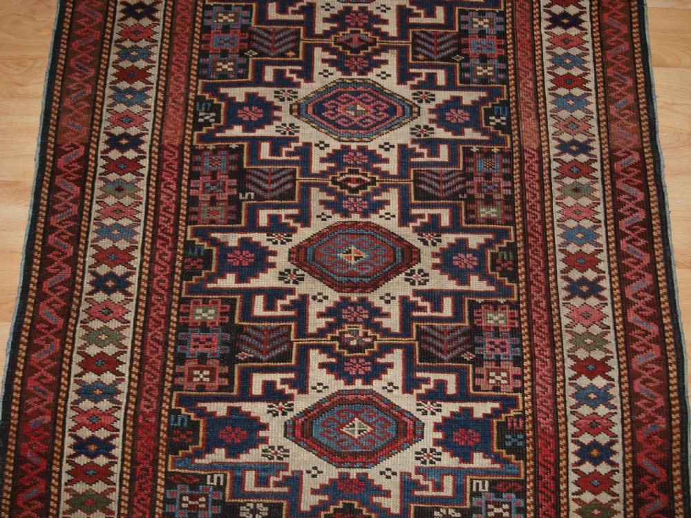 An antique Caucasian hand-knotted wool rug with geometric Lesghi star medallions on a cream field surrounded by patterned borders in red, navy, and ivory. View V