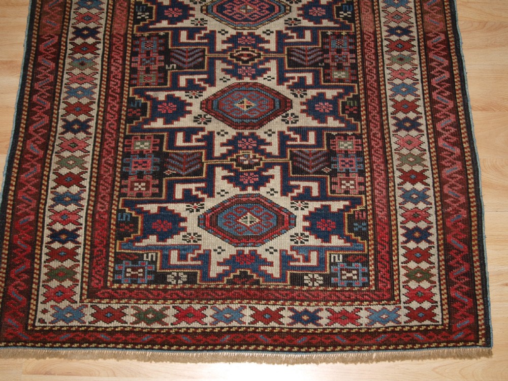 An antique Caucasian hand-knotted wool rug with geometric Lesghi star medallions on a cream field surrounded by patterned borders in red, navy, and ivory. View VI