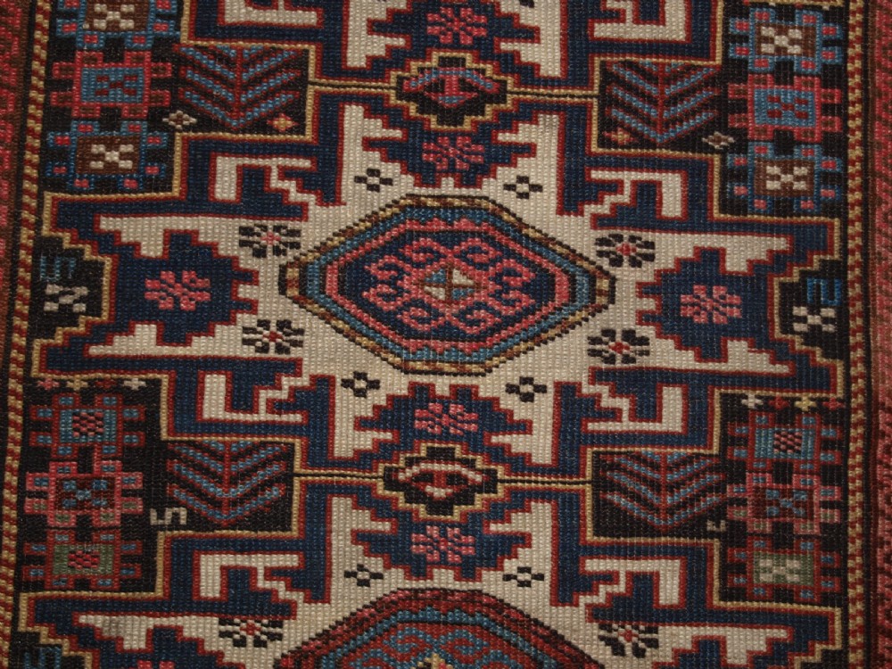 An antique Caucasian hand-knotted wool rug with geometric Lesghi star medallions on a cream field surrounded by patterned borders in red, navy, and ivory. View VII