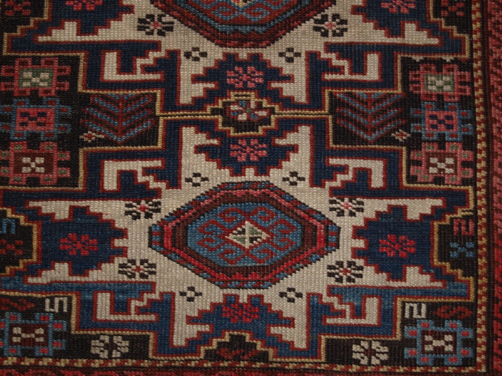 An antique Caucasian hand-knotted wool rug with geometric Lesghi star medallions on a cream field surrounded by patterned borders in red, navy, and ivory. View VIII