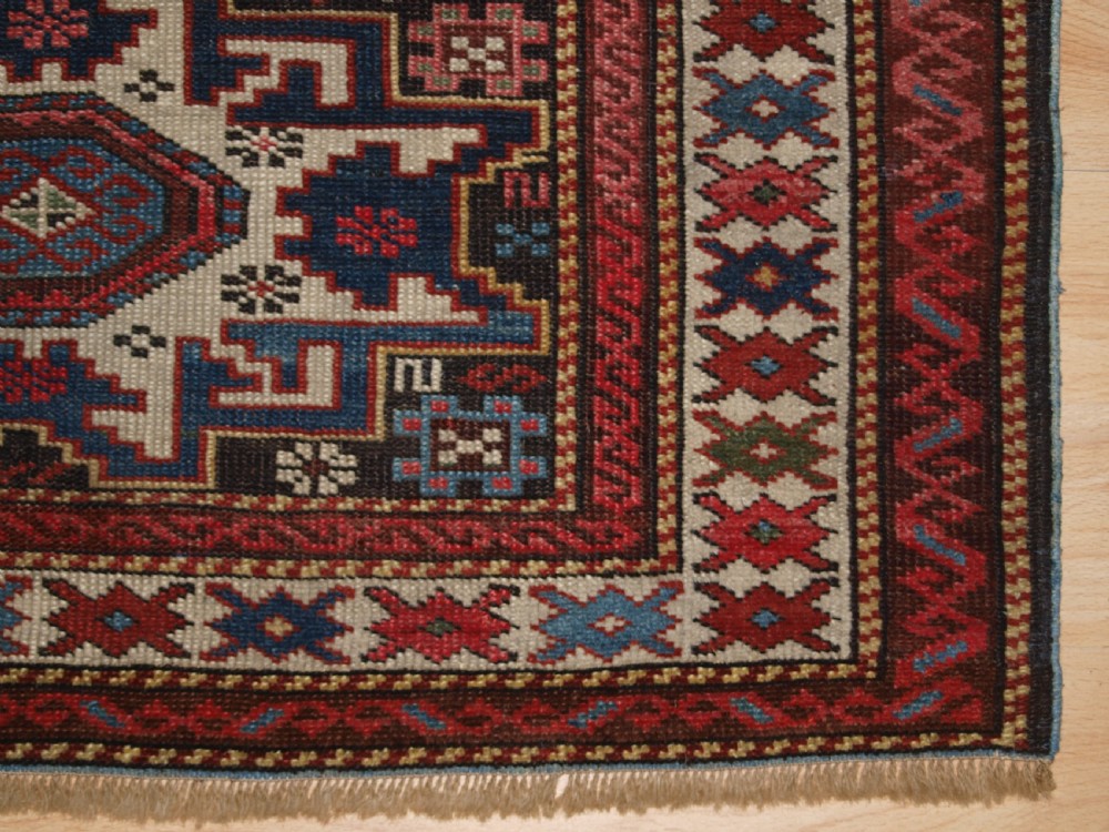 An antique Caucasian hand-knotted wool rug with geometric Lesghi star medallions on a cream field surrounded by patterned borders in red, navy, and ivory. View IX
