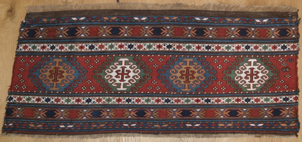 A rectangular hand-woven antique Caucasian Soumak wool panel featuring horizontal bands with geometric diamond medallions in terracotta red, navy blue, ivory, and green.