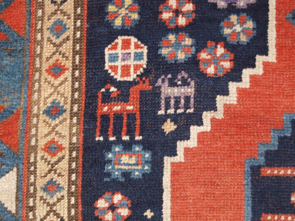 An antique hand-knotted Caucasian wool rug featuring red geometric diamond medallions on an indigo blue field with small human and animal figures. View XI