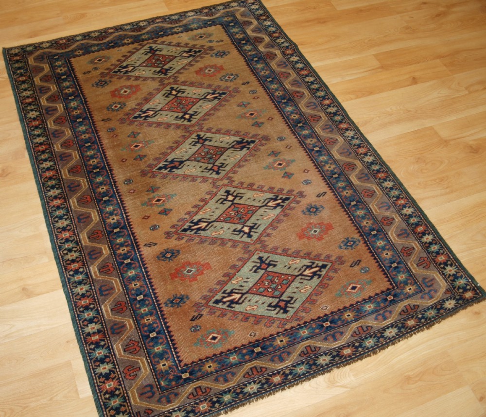 An antique Caucasian Derbent hand-knotted wool rug featuring five repeating diamond medallions in soft green and terracotta on a camel brown field with a geometric border. View II