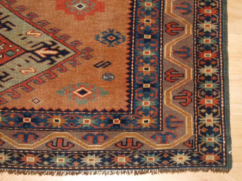 An antique Caucasian Derbent hand-knotted wool rug featuring five repeating diamond medallions in soft green and terracotta on a camel brown field with a geometric border. View VIII