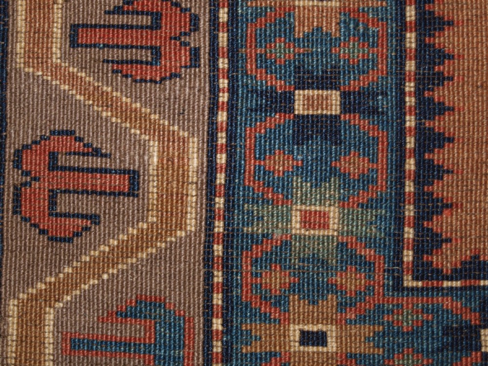 An antique Caucasian Derbent hand-knotted wool rug featuring five repeating diamond medallions in soft green and terracotta on a camel brown field with a geometric border. View X