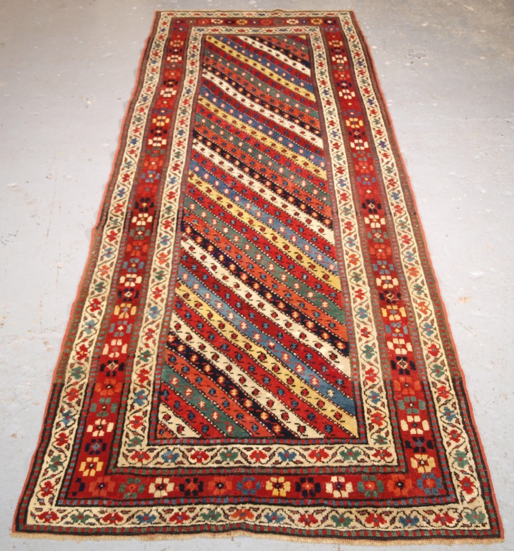 An antique handwoven wool Caucasian Gendje rug runner featuring diagonal polychrome stripes framed by multiple geometric borders.