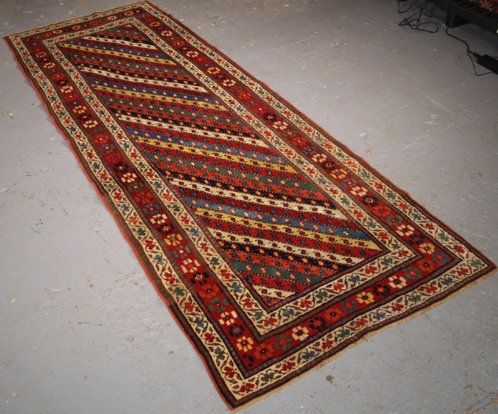 An antique handwoven wool Caucasian Gendje rug runner featuring diagonal polychrome stripes framed by multiple geometric borders. View II