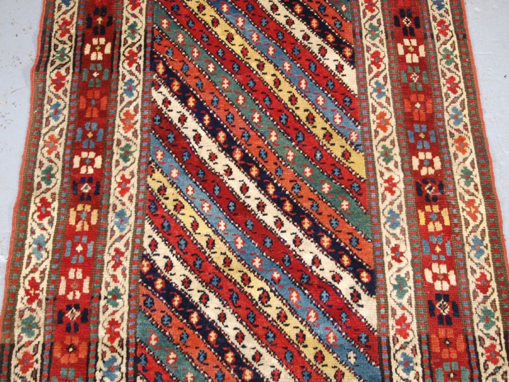 An antique handwoven wool Caucasian Gendje rug runner featuring diagonal polychrome stripes framed by multiple geometric borders. View V