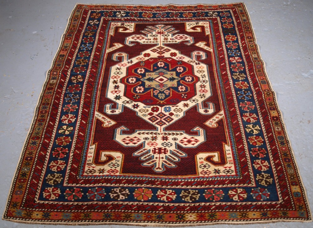 An antique Caucasian Shirvan wool rug featuring a central ivory and deep red Gymyl medallion surrounded by a dark blue rosette border.