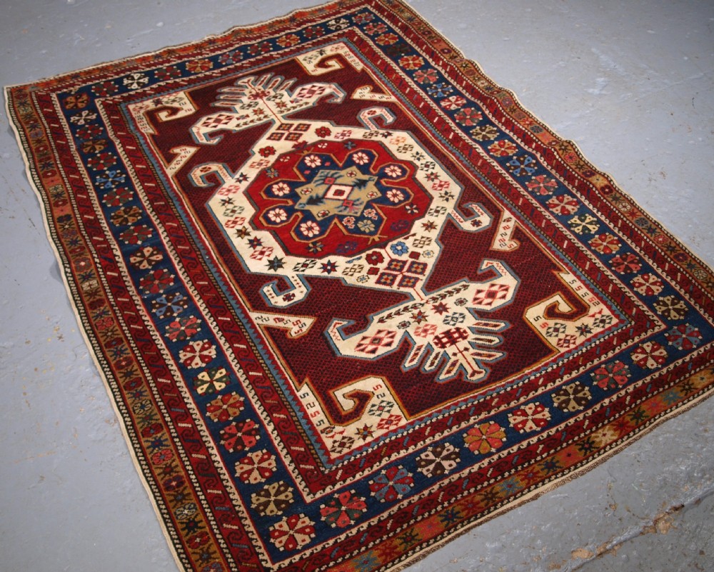An antique Caucasian Shirvan wool rug featuring a central ivory and deep red Gymyl medallion surrounded by a dark blue rosette border. View II