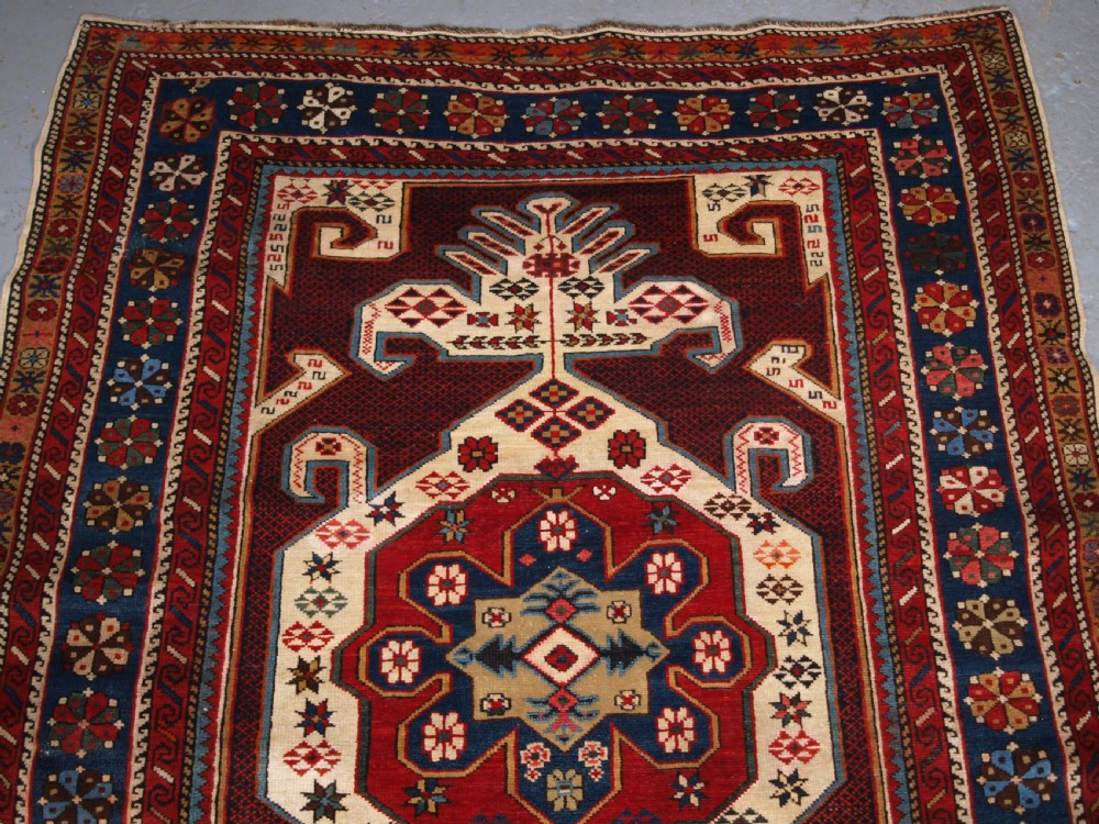 An antique Caucasian Shirvan wool rug featuring a central ivory and deep red Gymyl medallion surrounded by a dark blue rosette border. View III