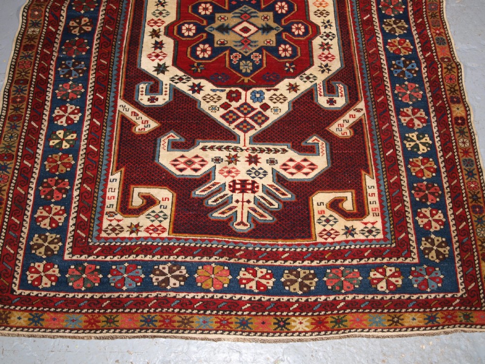 An antique Caucasian Shirvan wool rug featuring a central ivory and deep red Gymyl medallion surrounded by a dark blue rosette border. View V