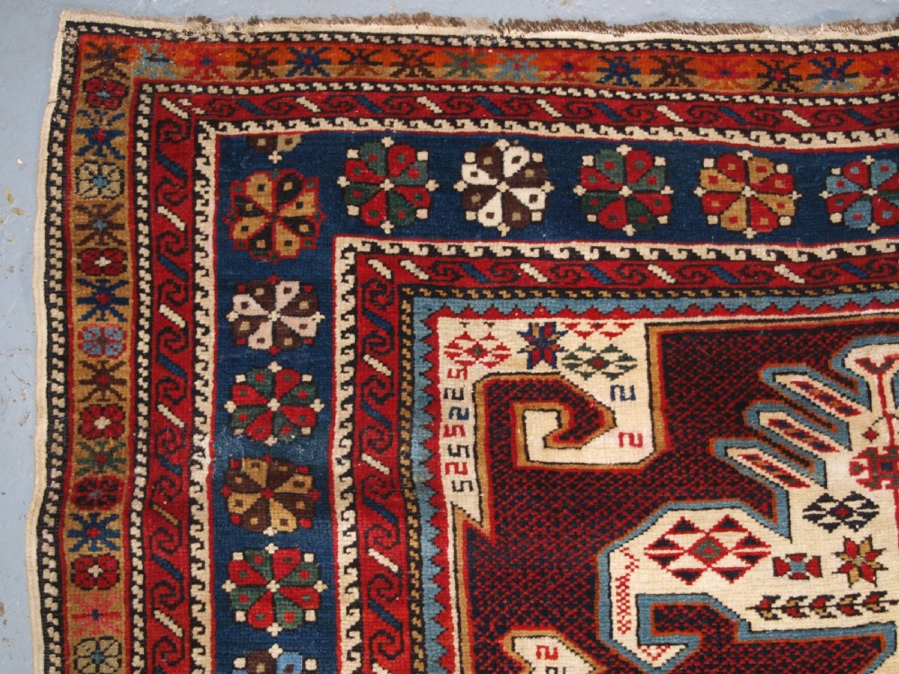 An antique Caucasian Shirvan wool rug featuring a central ivory and deep red Gymyl medallion surrounded by a dark blue rosette border. View VI