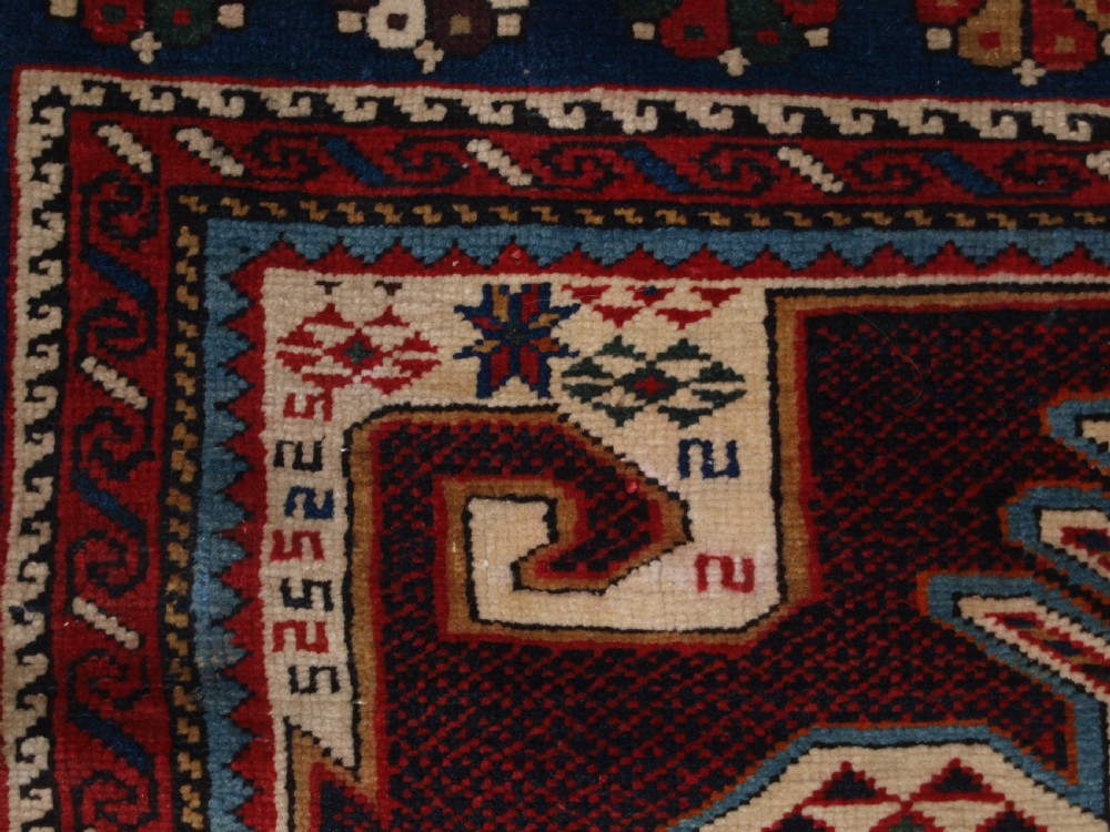 An antique Caucasian Shirvan wool rug featuring a central ivory and deep red Gymyl medallion surrounded by a dark blue rosette border. View VII