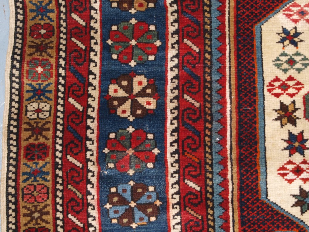 An antique Caucasian Shirvan wool rug featuring a central ivory and deep red Gymyl medallion surrounded by a dark blue rosette border. View VIII