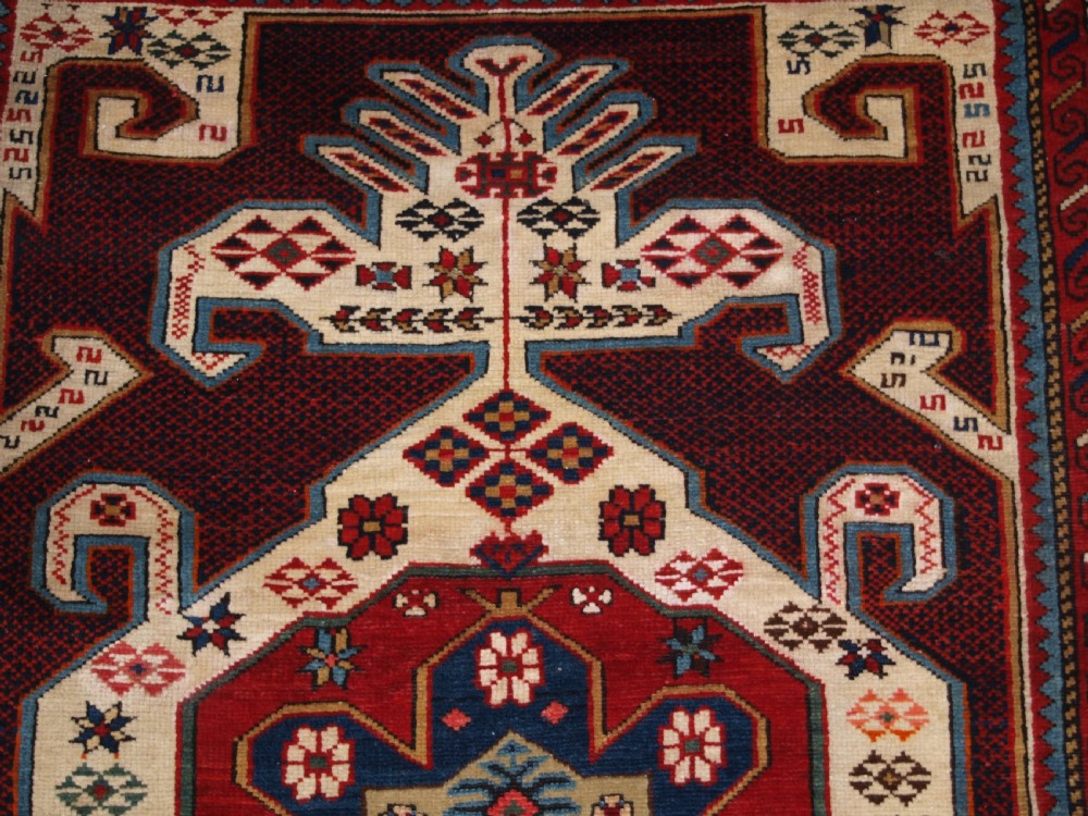 An antique Caucasian Shirvan wool rug featuring a central ivory and deep red Gymyl medallion surrounded by a dark blue rosette border. View IX