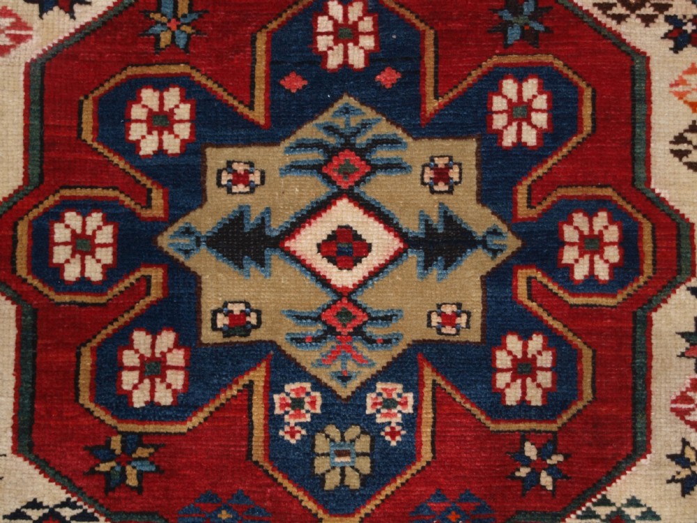 An antique Caucasian Shirvan wool rug featuring a central ivory and deep red Gymyl medallion surrounded by a dark blue rosette border. View X