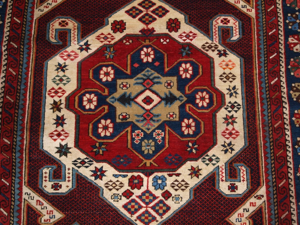 An antique Caucasian Shirvan wool rug featuring a central ivory and deep red Gymyl medallion surrounded by a dark blue rosette border. View XI