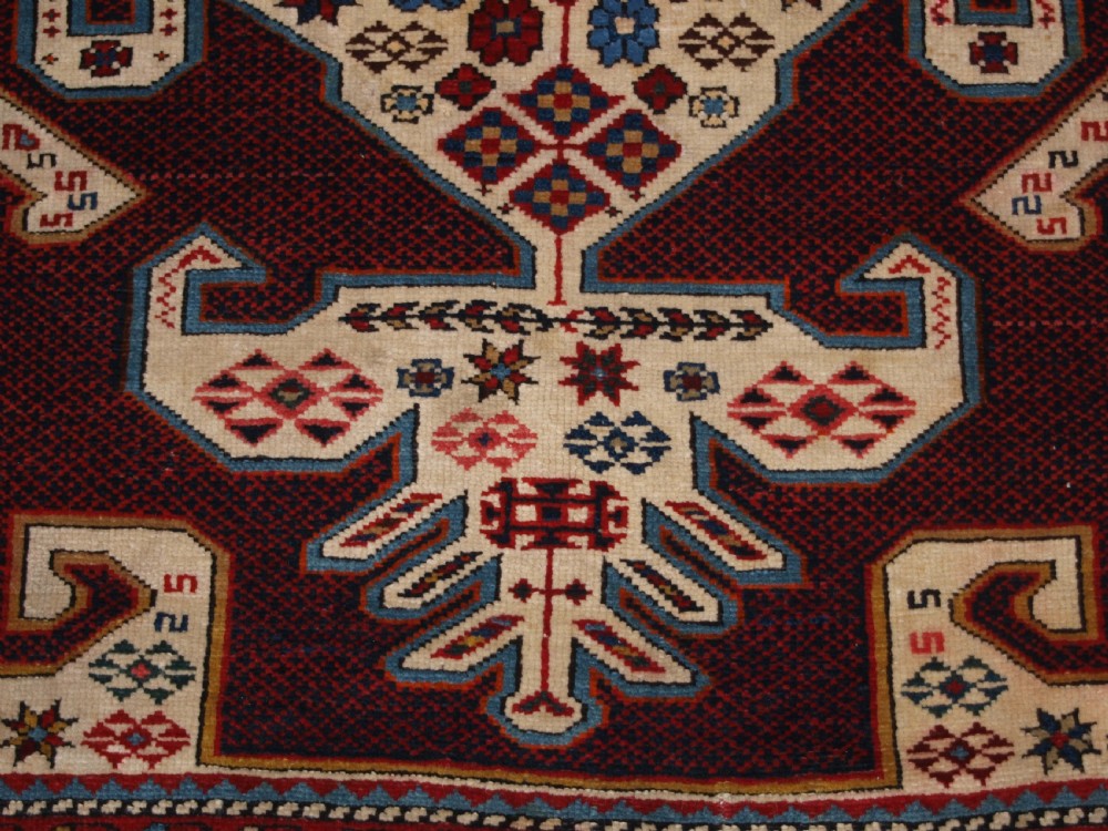 An antique Caucasian Shirvan wool rug featuring a central ivory and deep red Gymyl medallion surrounded by a dark blue rosette border. View XIII