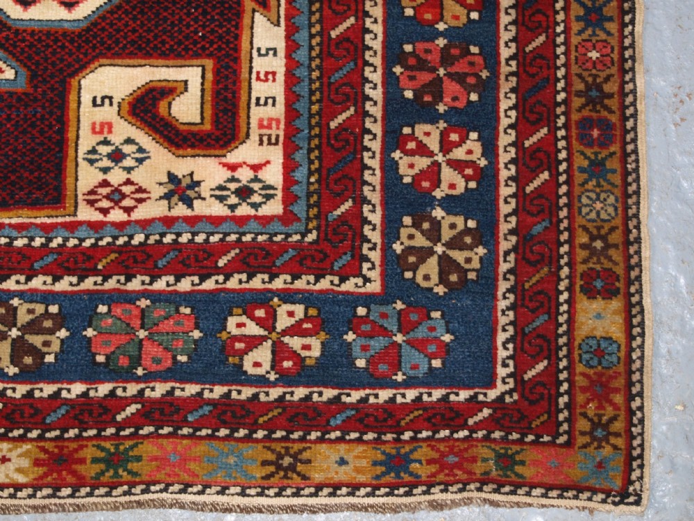 An antique Caucasian Shirvan wool rug featuring a central ivory and deep red Gymyl medallion surrounded by a dark blue rosette border. View XIV