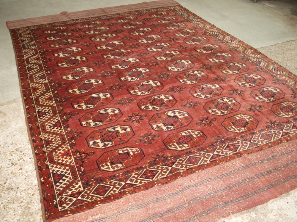 An antique red hand-knotted wool carpet displaying repeated octagonal gul motifs, geometric borders, and woven flatweave ends.