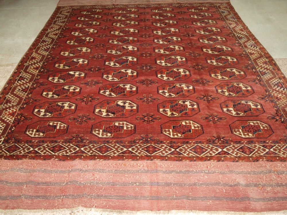 An antique red hand-knotted wool carpet displaying repeated octagonal gul motifs, geometric borders, and woven flatweave ends. View II