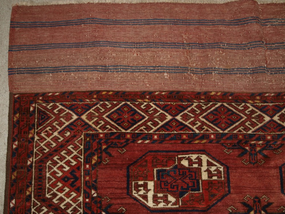 An antique red hand-knotted wool carpet displaying repeated octagonal gul motifs, geometric borders, and woven flatweave ends. View III