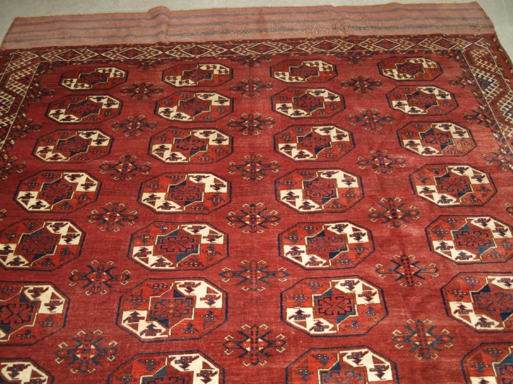 An antique red hand-knotted wool carpet displaying repeated octagonal gul motifs, geometric borders, and woven flatweave ends. View IV