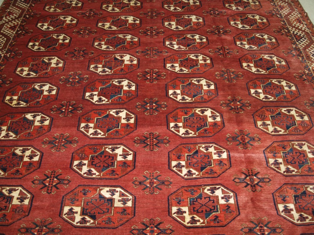 An antique red hand-knotted wool carpet displaying repeated octagonal gul motifs, geometric borders, and woven flatweave ends. View V