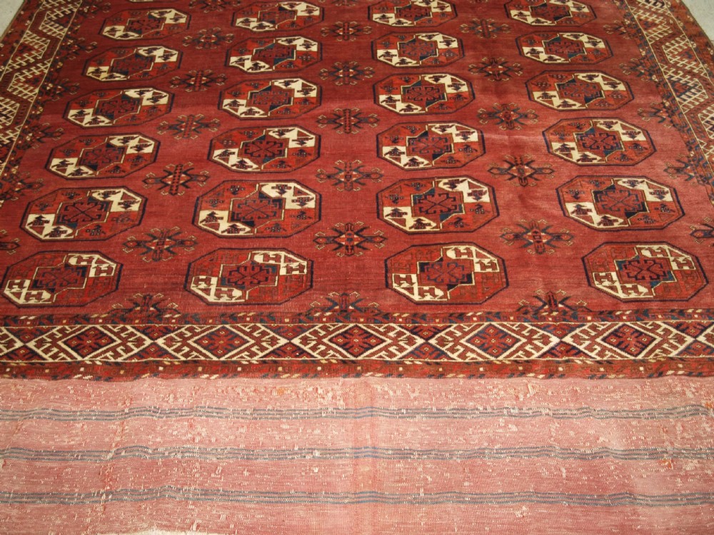 An antique red hand-knotted wool carpet displaying repeated octagonal gul motifs, geometric borders, and woven flatweave ends. View VI
