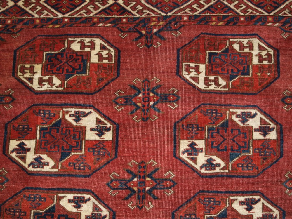An antique red hand-knotted wool carpet displaying repeated octagonal gul motifs, geometric borders, and woven flatweave ends. View VII