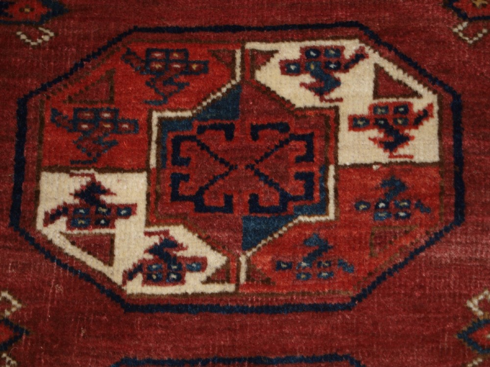 An antique red hand-knotted wool carpet displaying repeated octagonal gul motifs, geometric borders, and woven flatweave ends. View IX