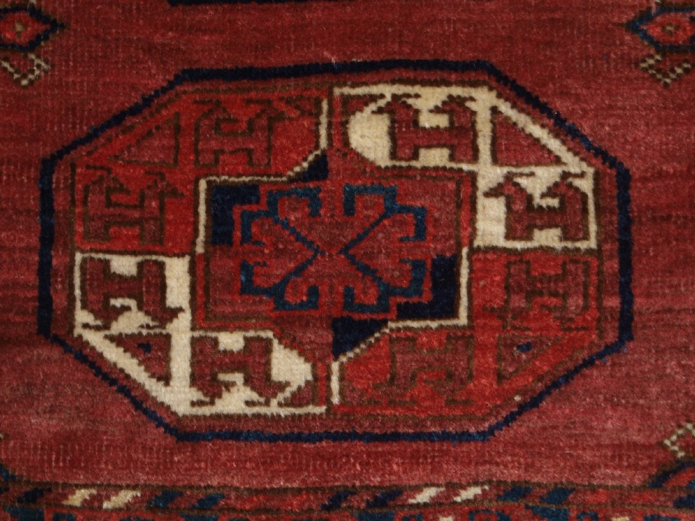An antique red hand-knotted wool carpet displaying repeated octagonal gul motifs, geometric borders, and woven flatweave ends. View X