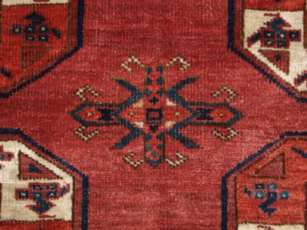 An antique red hand-knotted wool carpet displaying repeated octagonal gul motifs, geometric borders, and woven flatweave ends. View XII