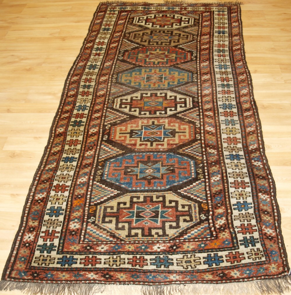 An antique hand-knotted Kurdish runner rug featuring a vertical sequence of octagonal Memling gul motifs in terracotta, blue, and cream shades.