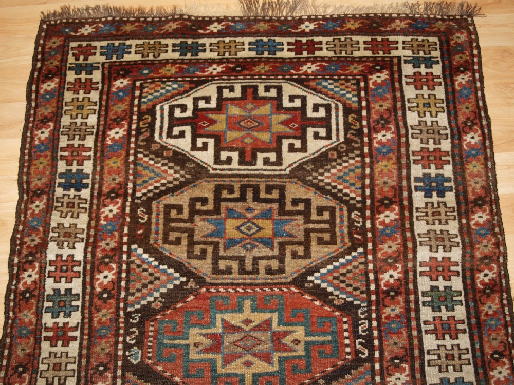 An antique hand-knotted Kurdish runner rug featuring a vertical sequence of octagonal Memling gul motifs in terracotta, blue, and cream shades. View III